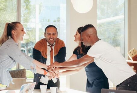 Structural Integrity - Content multiethnic colleagues joining hands above table with laptops in modern office on sunny day