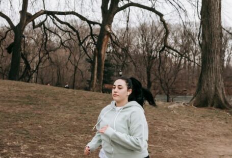 Rotational Dynamics - Full body motivated plus sized female in gray hoodie running in autumn park